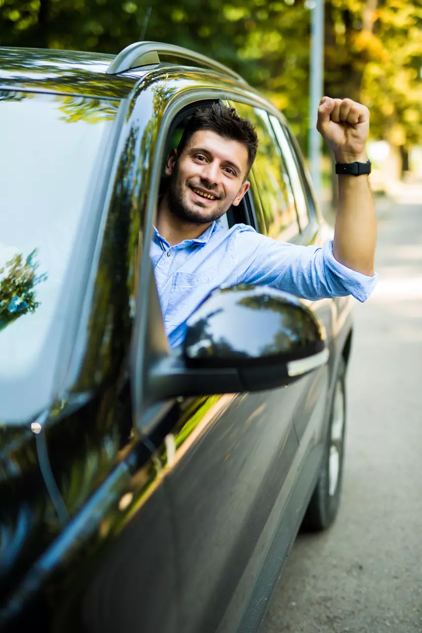 young man raising his fist up from car